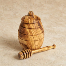 Small handmade olive wood honey jar with dipper featuring natural grain and warm golden brown olive wood honey tones