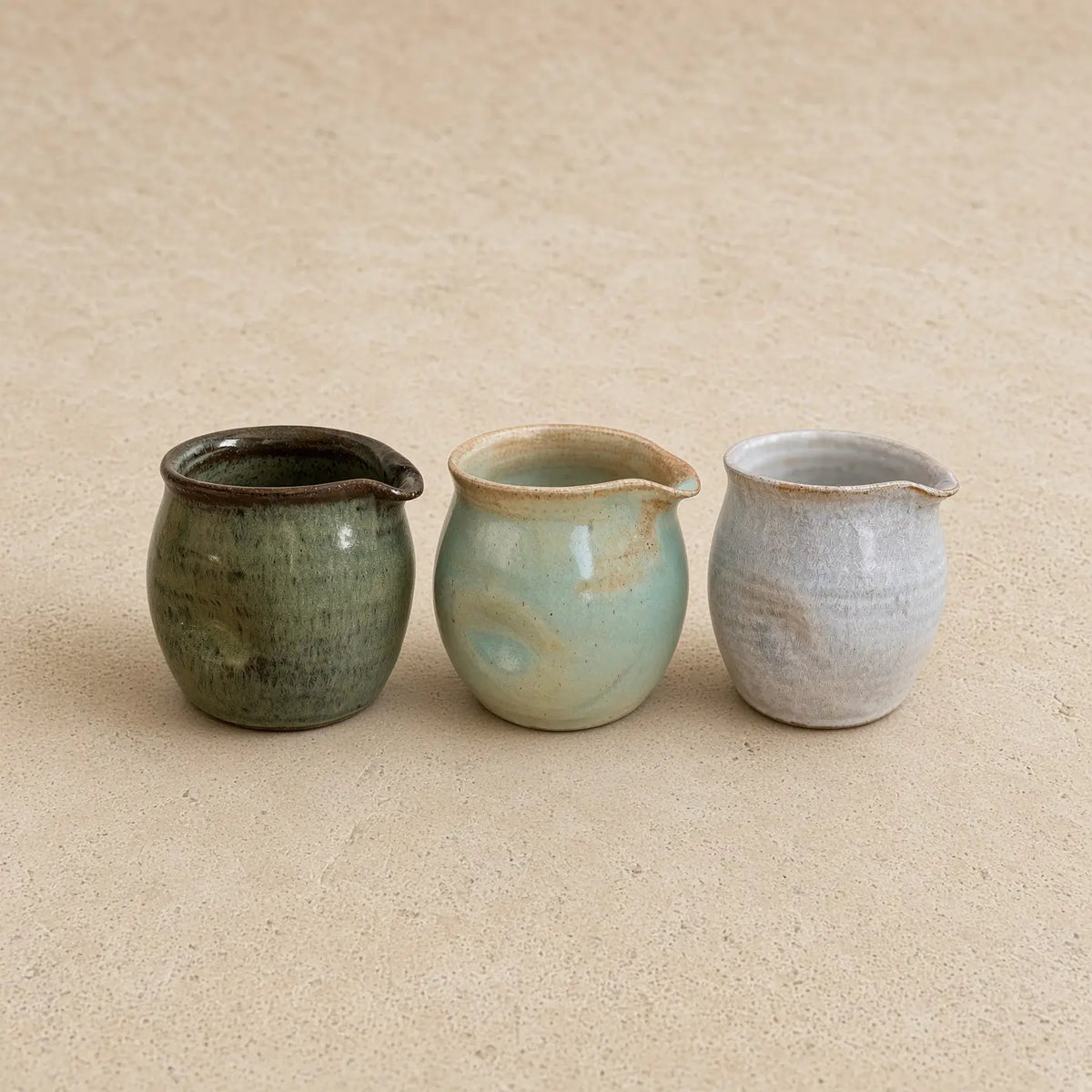 Three small thumb divot handmade pitchers in muted green blue-green and pale gray perfect for pouring cream with awkward grip