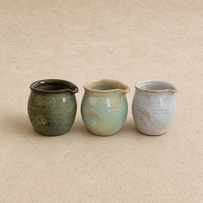 Three small thumb divot handmade pitchers in muted green blue-green and pale gray perfect for pouring cream with awkward grip