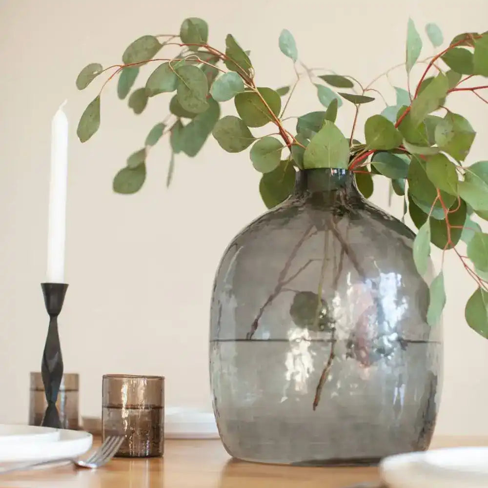 Handblown hammered glass vase in blue gray on wooden table with place setting.