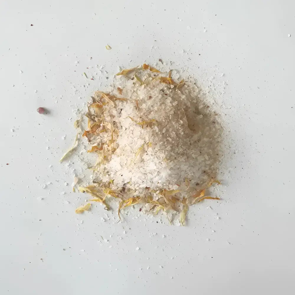 A mound of white coarse soaking salts mixed with dried orange and yellow flower petals for western herbalism use
