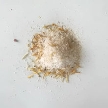 A mound of white coarse soaking salts mixed with dried orange and yellow flower petals for western herbalism use