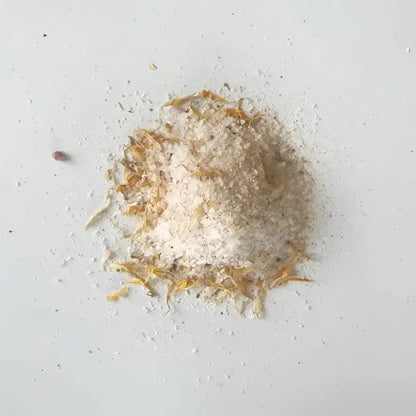 A mound of white coarse soaking salts mixed with dried orange and yellow flower petals for western herbalism use