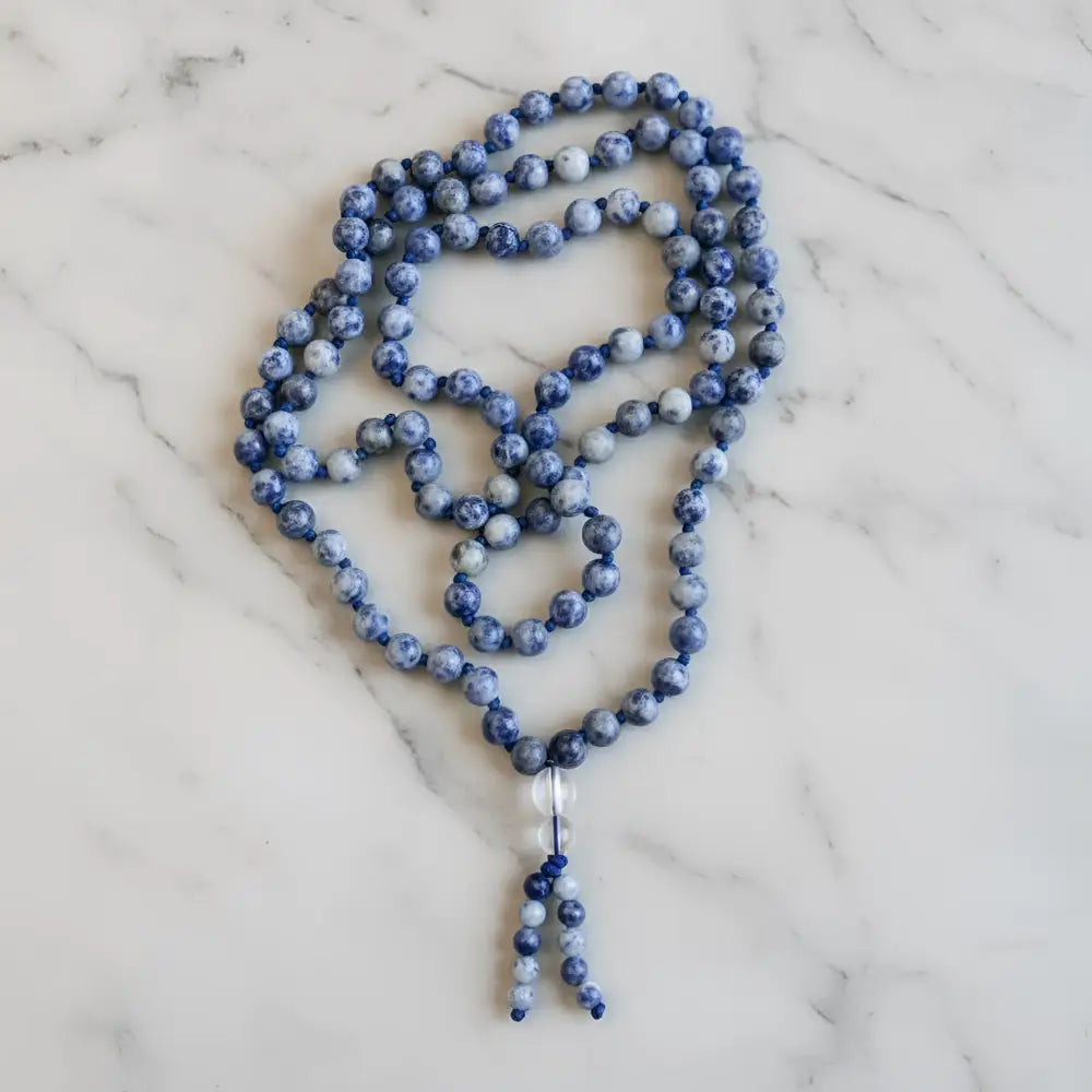 A blue and white speckled sodalite beads mala with clear crystal pendant perfect for mantra chanting and meditation companion