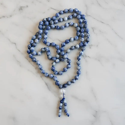 A blue and white speckled sodalite beads mala with clear crystal pendant perfect for mantra chanting and meditation companion