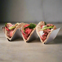 Stainless steel upright taco rack holding three steak tacos with radishes and herbs