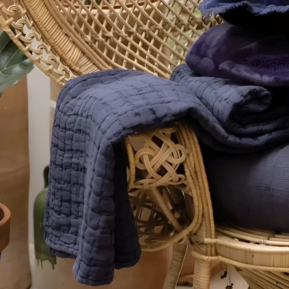 Navy quilt draped over a wicker chair with a blurred natural background