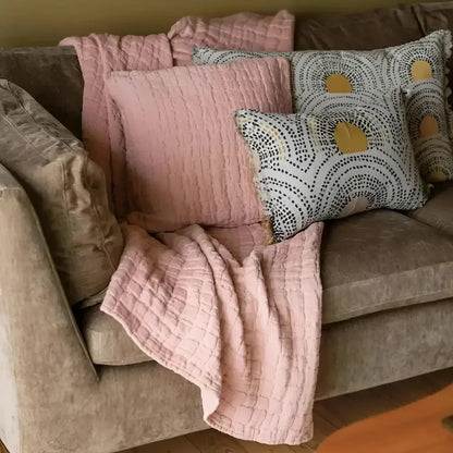 Cozy living room scene with a beige sofa adorned with clay textured pillows and a blanket.