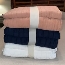 Stack of folded blankets in clay, white, and navy on a bed.