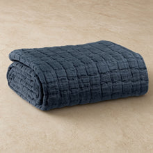 A neatly folded navy blue stonewashed cotton lightweight quilt with a textured grid pattern king size quilt option