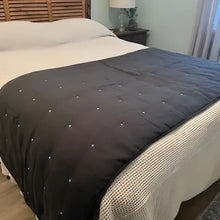 Dark gray quilt with button details on a bed in a bedroom setting