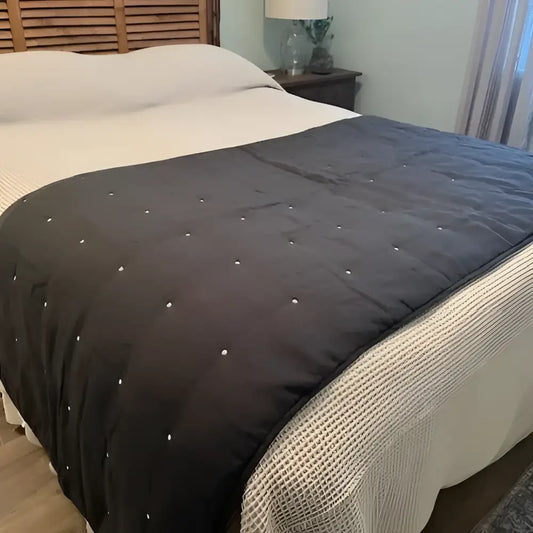 Dark gray quilt with button details on a bed in a bedroom setting