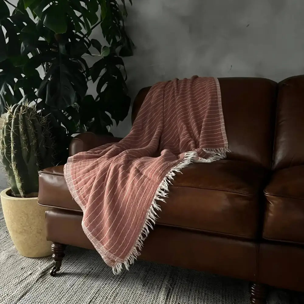 Pink striped Turkish cotton blanket with fringe draped over a brown leather sofa