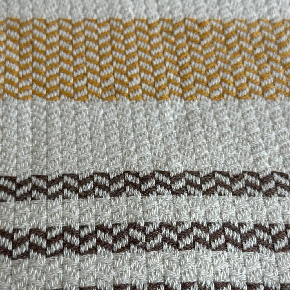 Turkish cotton blanket with a natural, cream colored cotton base woven in an understated modern herringbone pattern with stripes and pom pom edging.