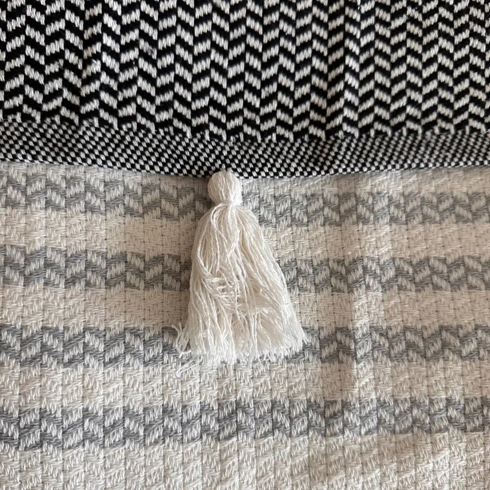 Turkish cotton blanket with a natural, cream colored cotton base woven in an understated modern herringbone pattern with stripes and pom pom edging.