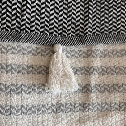 Turkish cotton blanket with a natural, cream colored cotton base woven in an understated modern herringbone pattern with stripes and pom pom edging.
