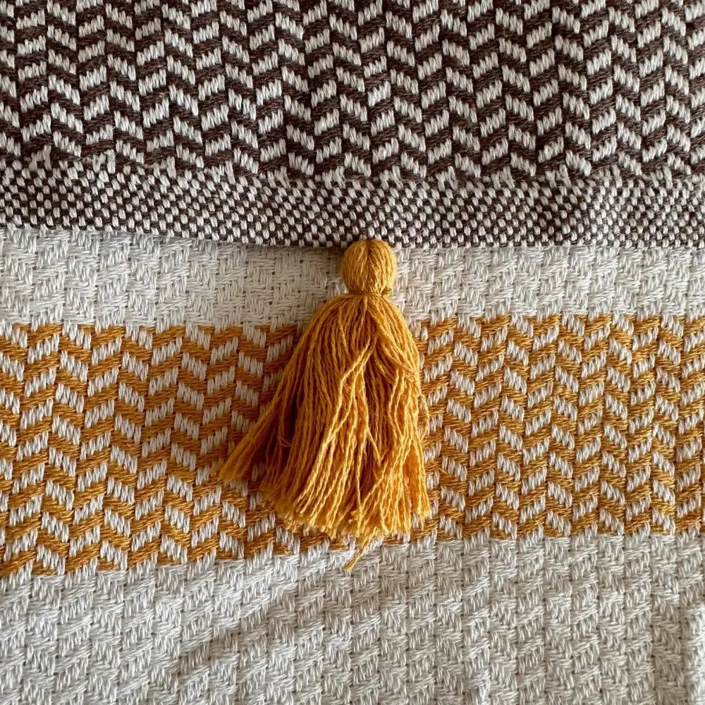Turkish cotton blanket with a natural, cream colored cotton base woven in an understated modern herringbone pattern with stripes and pom pom edging.