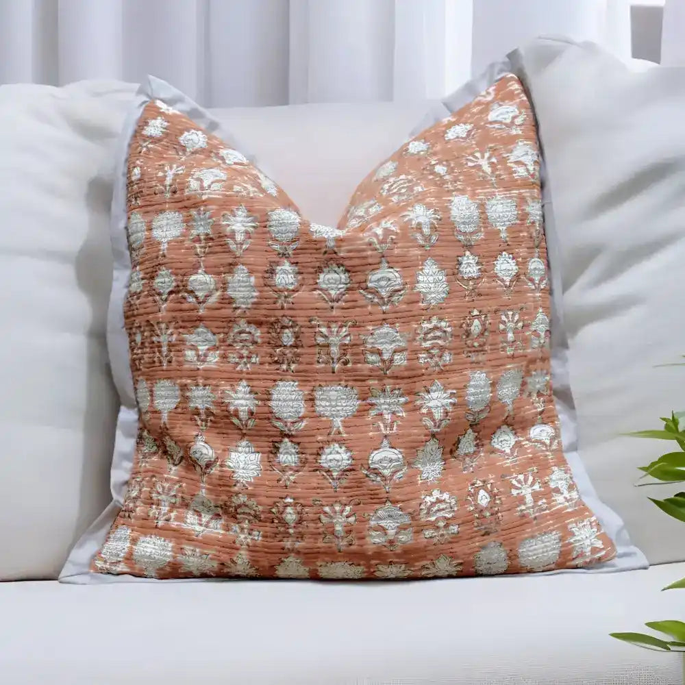 Pillow cover features a rusty-peach colored cotton gauze material with a hand block print design in a neutral color and has a zipper closure on the back side.