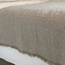 A linen bed runner with a frayed woven design in beige.