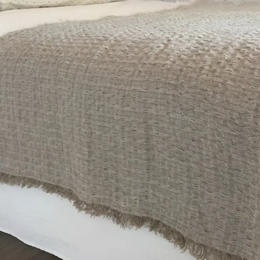 A linen bed runner with a frayed woven design in beige.