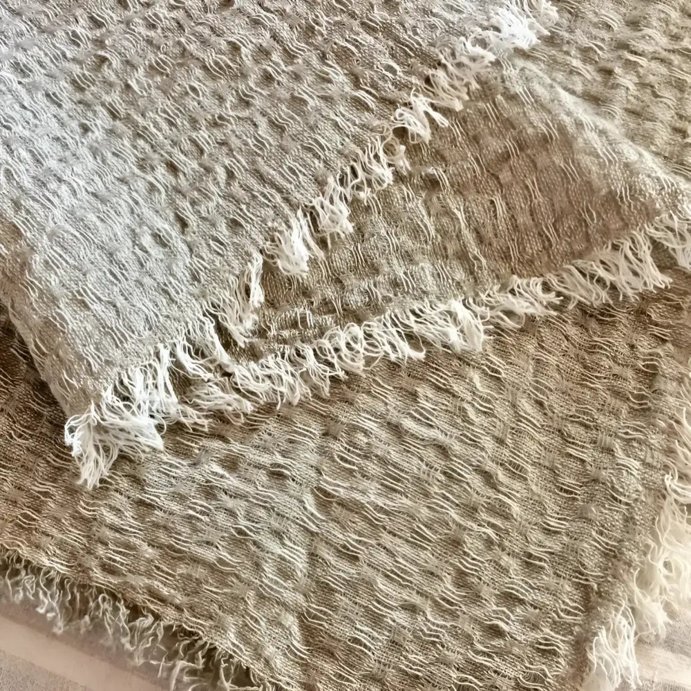 A linen bed runner with a frayed woven design in beige.
