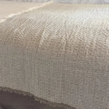 A linen bed runner with a frayed woven design in beige.