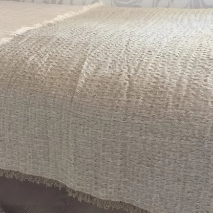 A linen bed runner with a frayed woven design in beige.