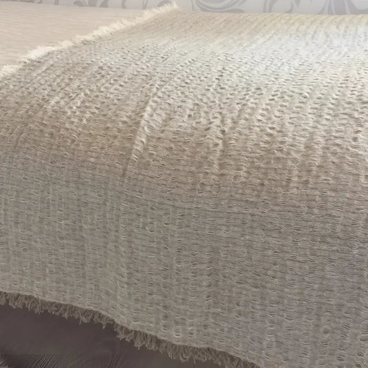 A linen bed runner with a frayed woven design in beige.