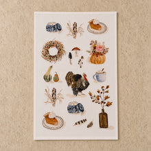 A cotton flour sack tea towel with autumn watercolor illustrations of pumpkins turkey and pie on white paper