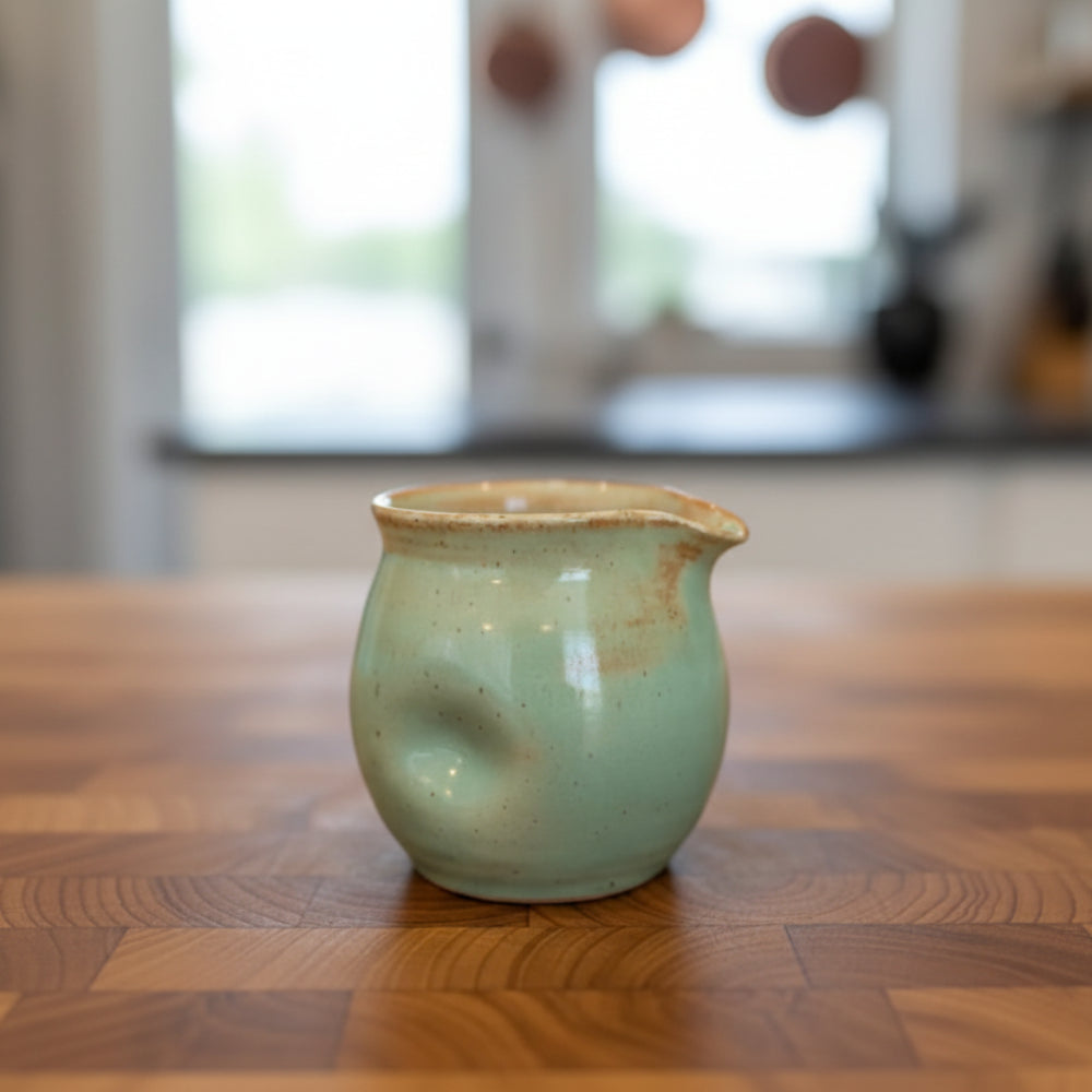 Handcrafted 8 oz thumb divot pitcher in teal glaze with brown rim