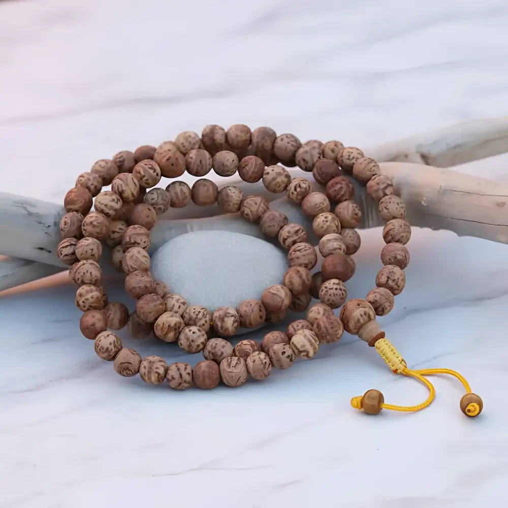 A coiled bodhi seed mala prayer beads with natural brown textured wooden beads and yellow cord carrying profound seed carries