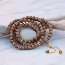 A coiled bodhi seed mala prayer beads with natural brown textured wooden beads and yellow cord carrying profound seed carries