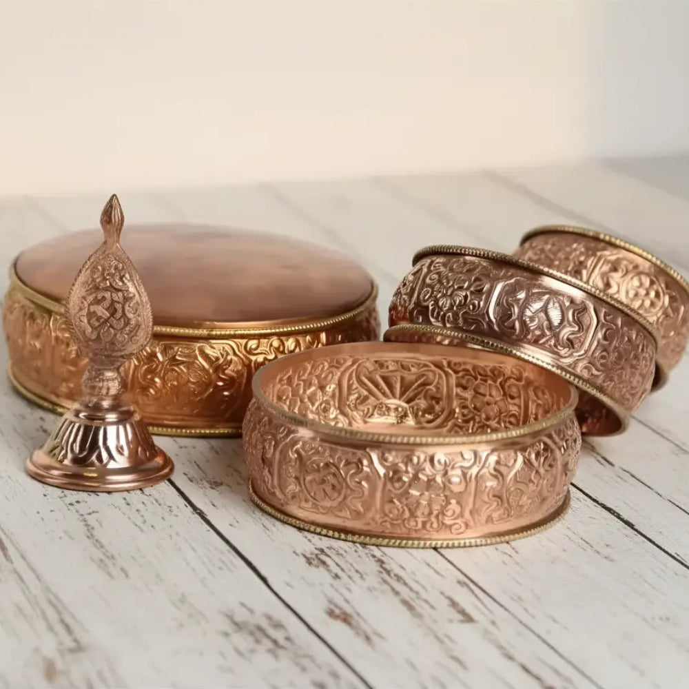 Copper-colored traditional tibetan buddhist prayer wheel with intricate engravings in an offering mandala set