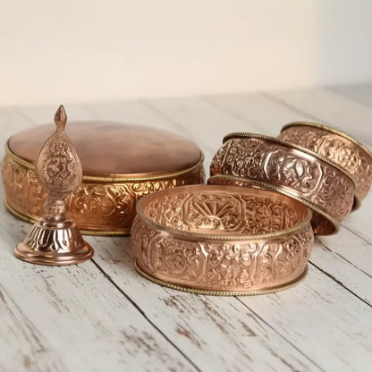 Copper-colored traditional tibetan buddhist prayer wheel with intricate engravings in an offering mandala set