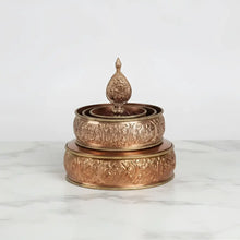 A copper-colored traditional tibetan buddhist offering mandala set featuring an intricately engraved prayer wheel with finial