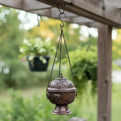 Antique bronze tibetan hanging incense burner with intricate floral scrollwork suspended by chain from wooden pergola