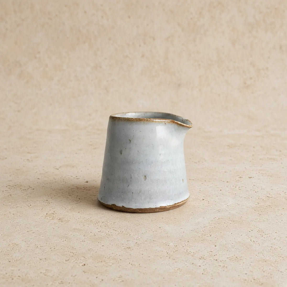 Tiny handmade ceramic condiment pitcher with matte light blue glaze and earthy brown rim for serving sauces