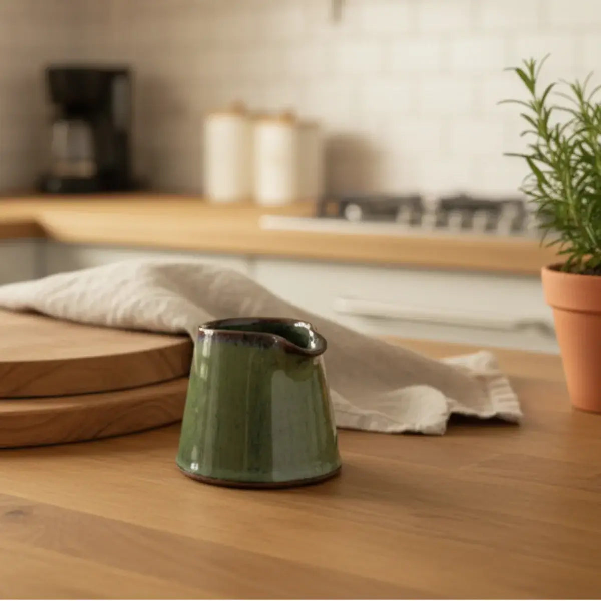 Tiny handmade ceramic condiment pitcher in olive green with a dark brown rim and handle perfect for sauces