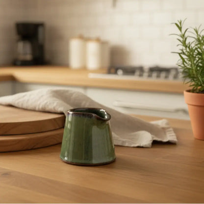 Tiny handmade ceramic condiment pitcher in olive green with a dark brown rim and handle perfect for sauces