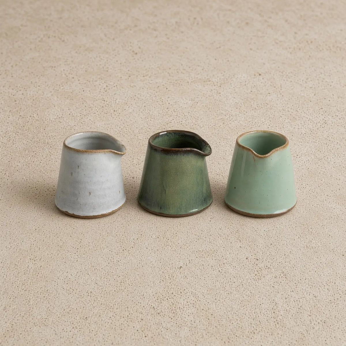 Three tiny handmade ceramic condiment pitchers in muted gray olive green and mint green with rustic brown rims