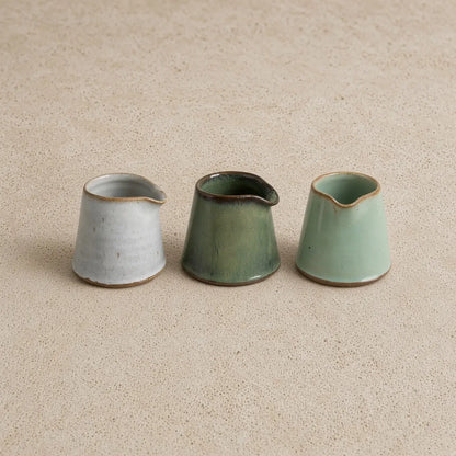 Three tiny handmade ceramic condiment pitchers in muted gray olive green and mint green with rustic brown rims