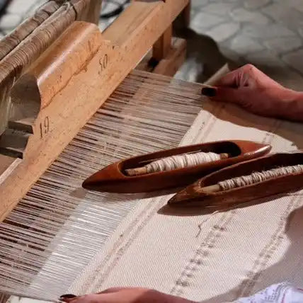 A traditional wooden handloom with two shuttles containing white thread.