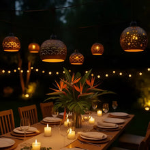 Warm amber glowing spherical pendant lights with hand carved coconut shades above candlelit outdoor table
