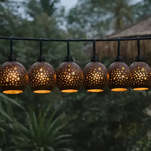 A string of warm-toned spherical outdoor lanterns with hand-carved coconut shades featuring star and dot cutouts