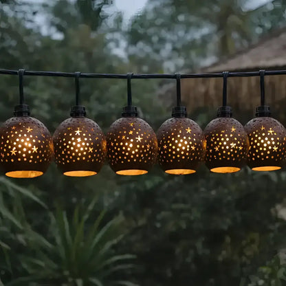 A string of warm-toned spherical outdoor lanterns with hand-carved coconut shades featuring star and dot cutouts