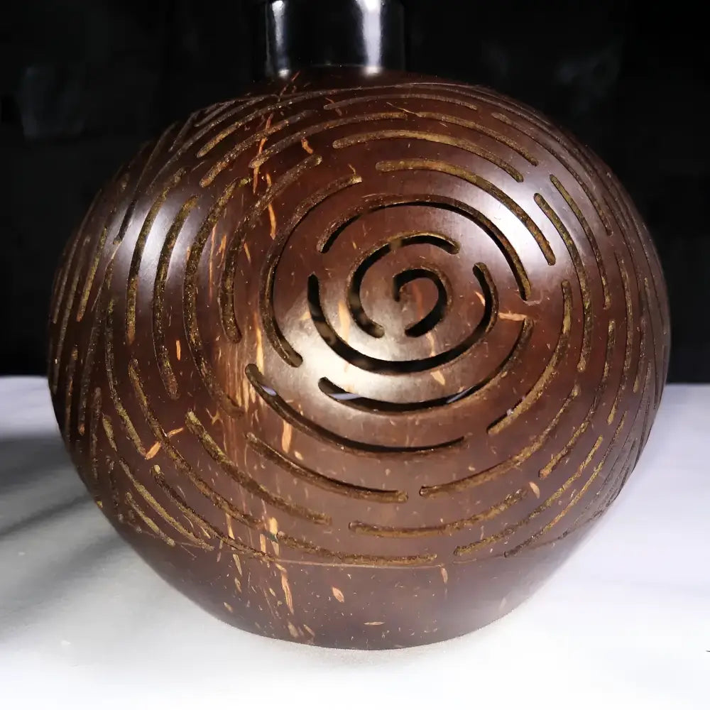 Dark brown hand-carved coconut shell lantern with intricate spiral cutouts featuring natural fiber texture for tropical patio use