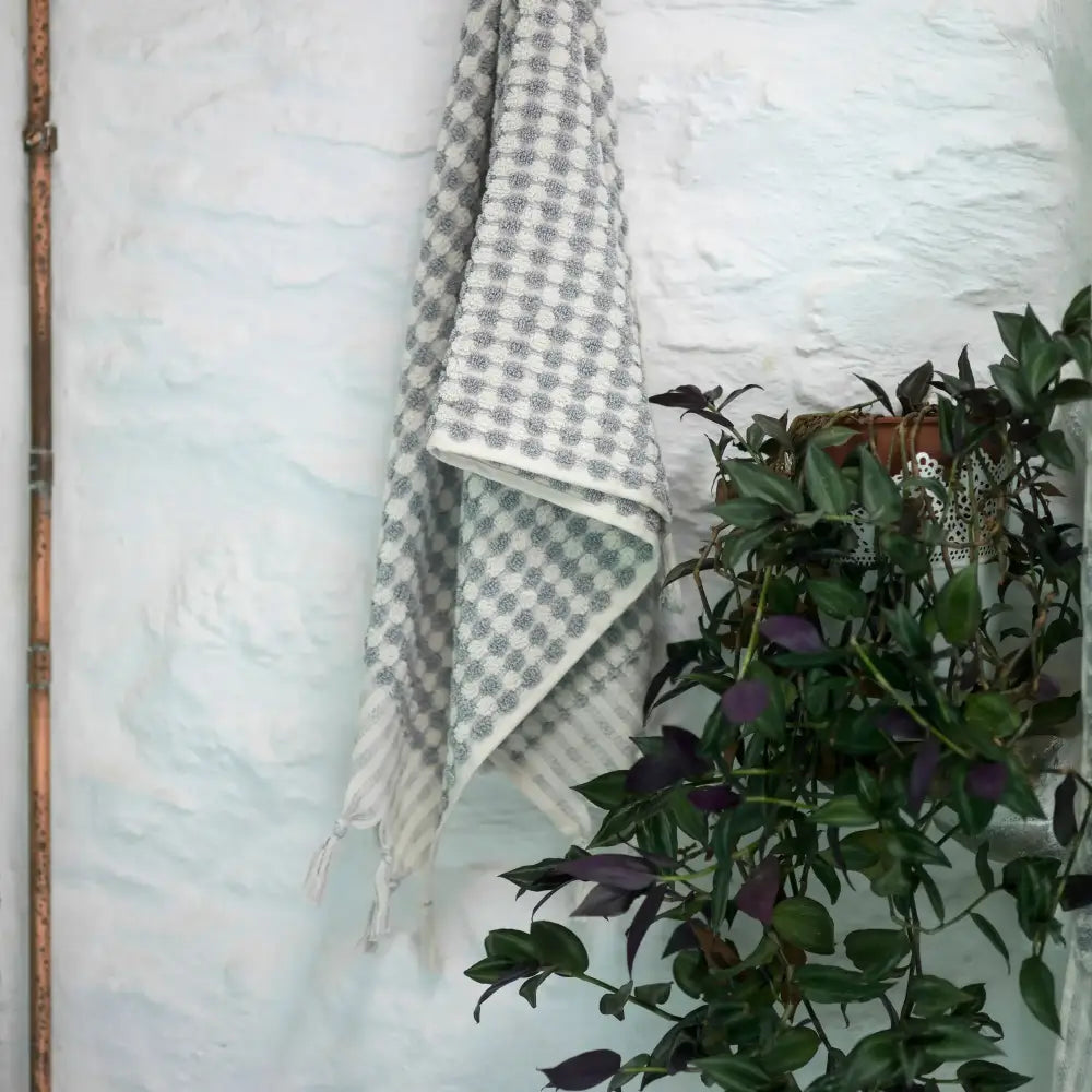 Light grey and white dotted Turkish cotton hand towel with tassels hanging on textured wall