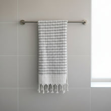 Light grey and white dotted Turkish cotton hand towel with tassels hanging on textured wall