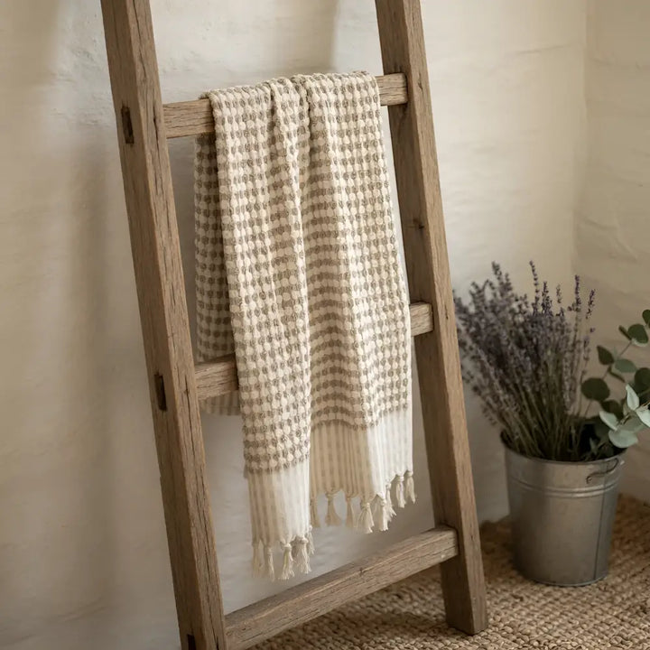Beige and cream turkish cotton dotted terry long hand towel with tassels hanging on wooden ladder