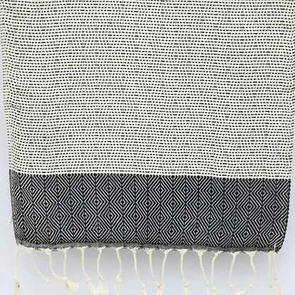 A turkish hand towel with diamonds and dots woven in black.